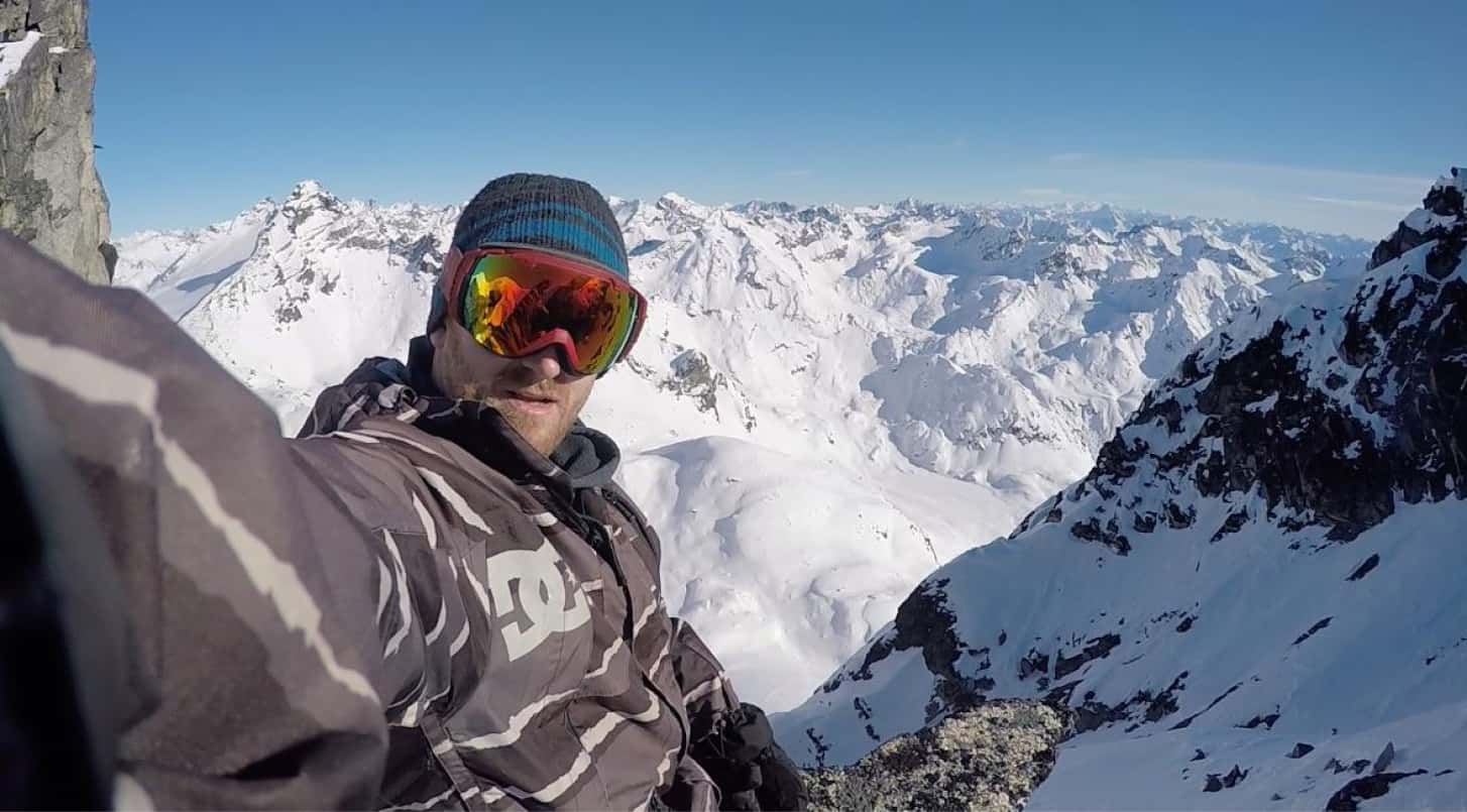 Picture of Kevin taking a selfie on the side of a mountain. He is dressed in full skiing gear with goggles pulled over his face.